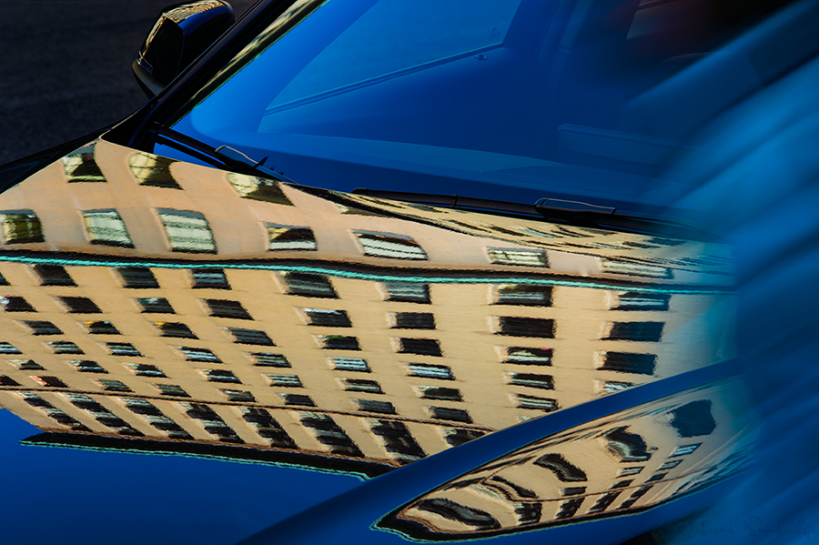 Reflections of NYC building on blue car.